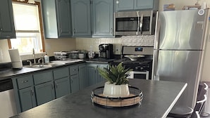 A modern kitchen with blue cabinets, a stainless steel refrigerator, and a central island with bar stools.