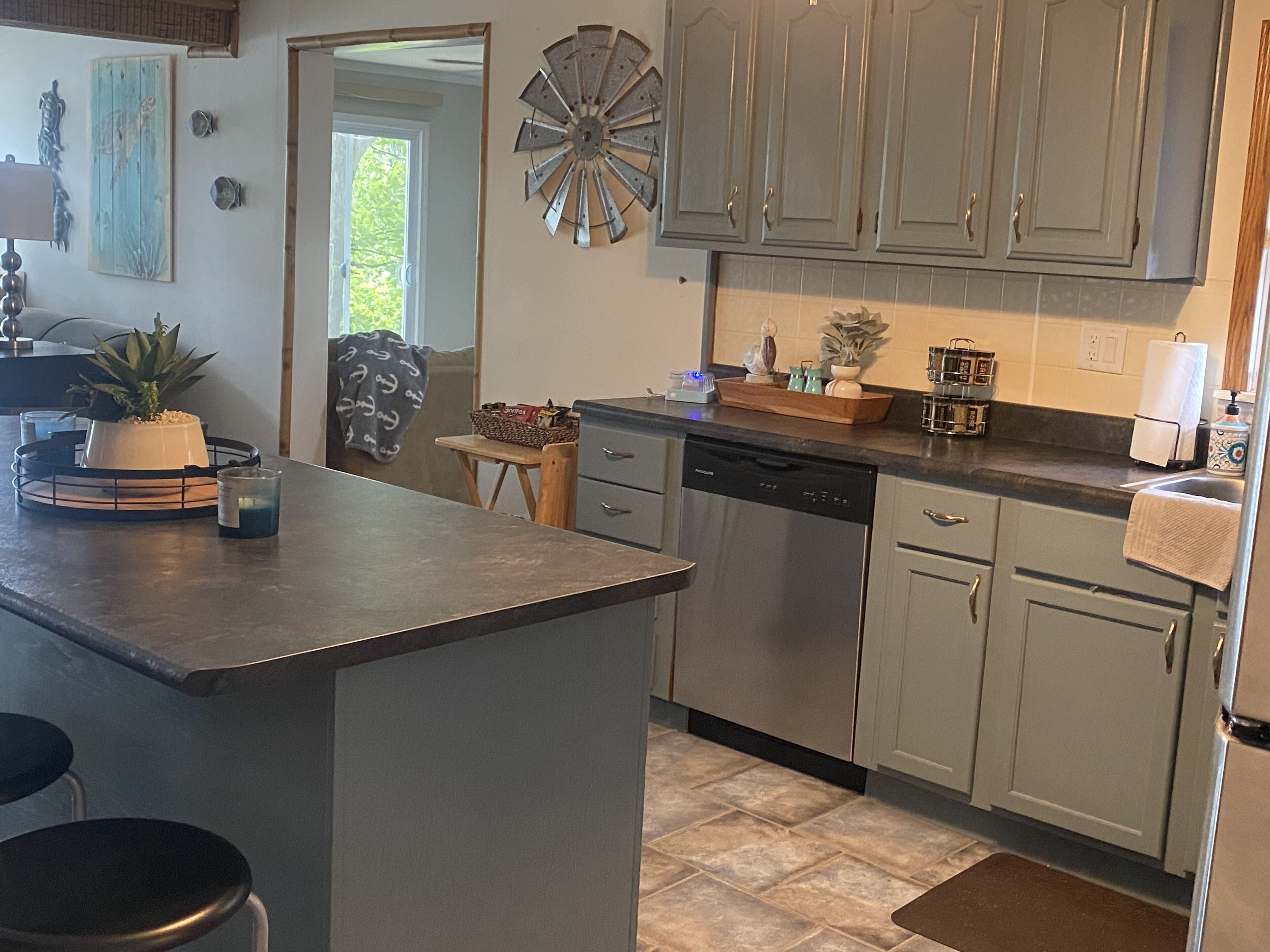 A kitchen with grey cabinets, a dishwasher, and a countertop with a plant and a basket.