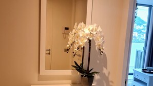 A white console table with a potted orchid, a mirror above it, and a geometric-patterned drawer unit.