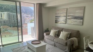 A modern living room with a sofa, a coffee table, and a view of a cityscape through large windows.