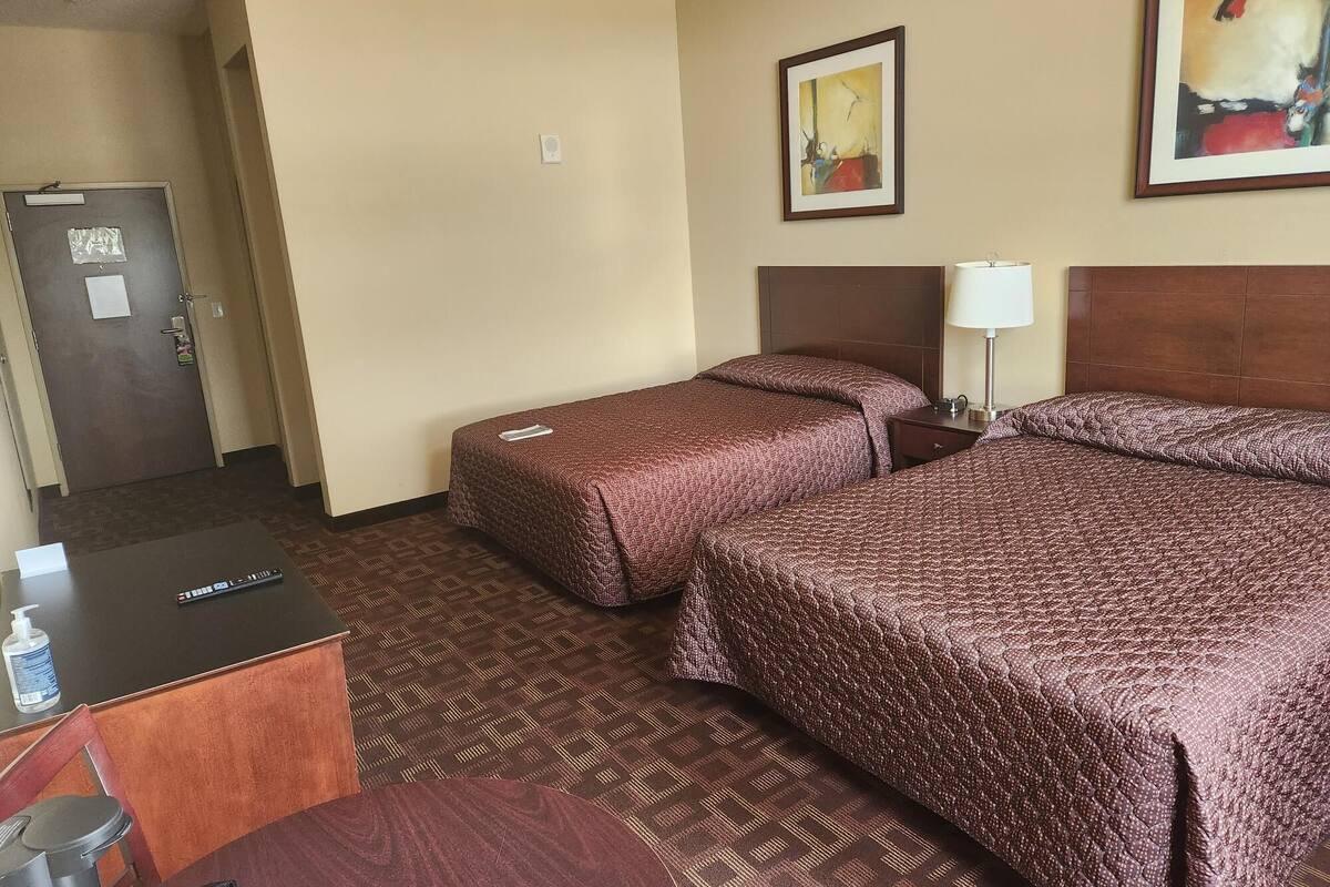 A hotel room with two beds, a desk, a chair, and a door.