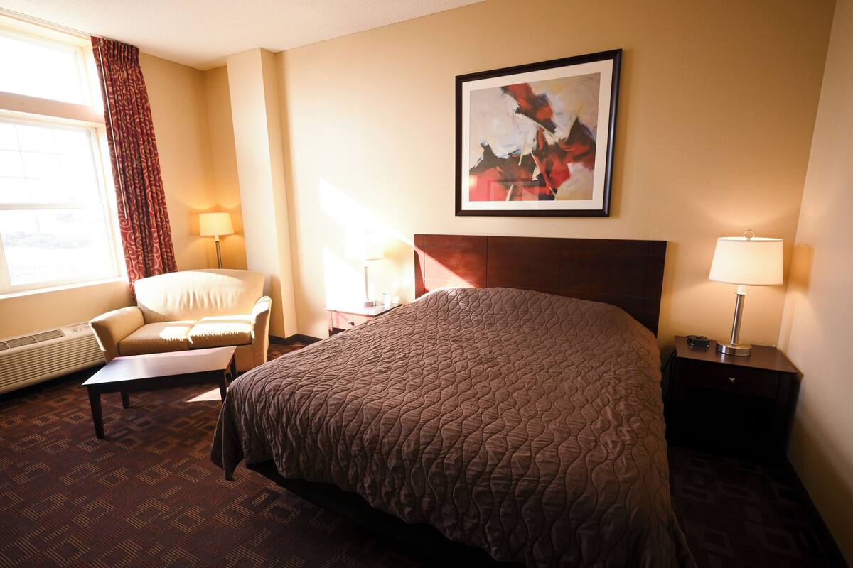 A hotel room with a large bed, a chair, a desk, and a nightstand with lamps.