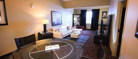 A hotel room with a glass dining table, a sofa, a TV, and a patterned carpet.
