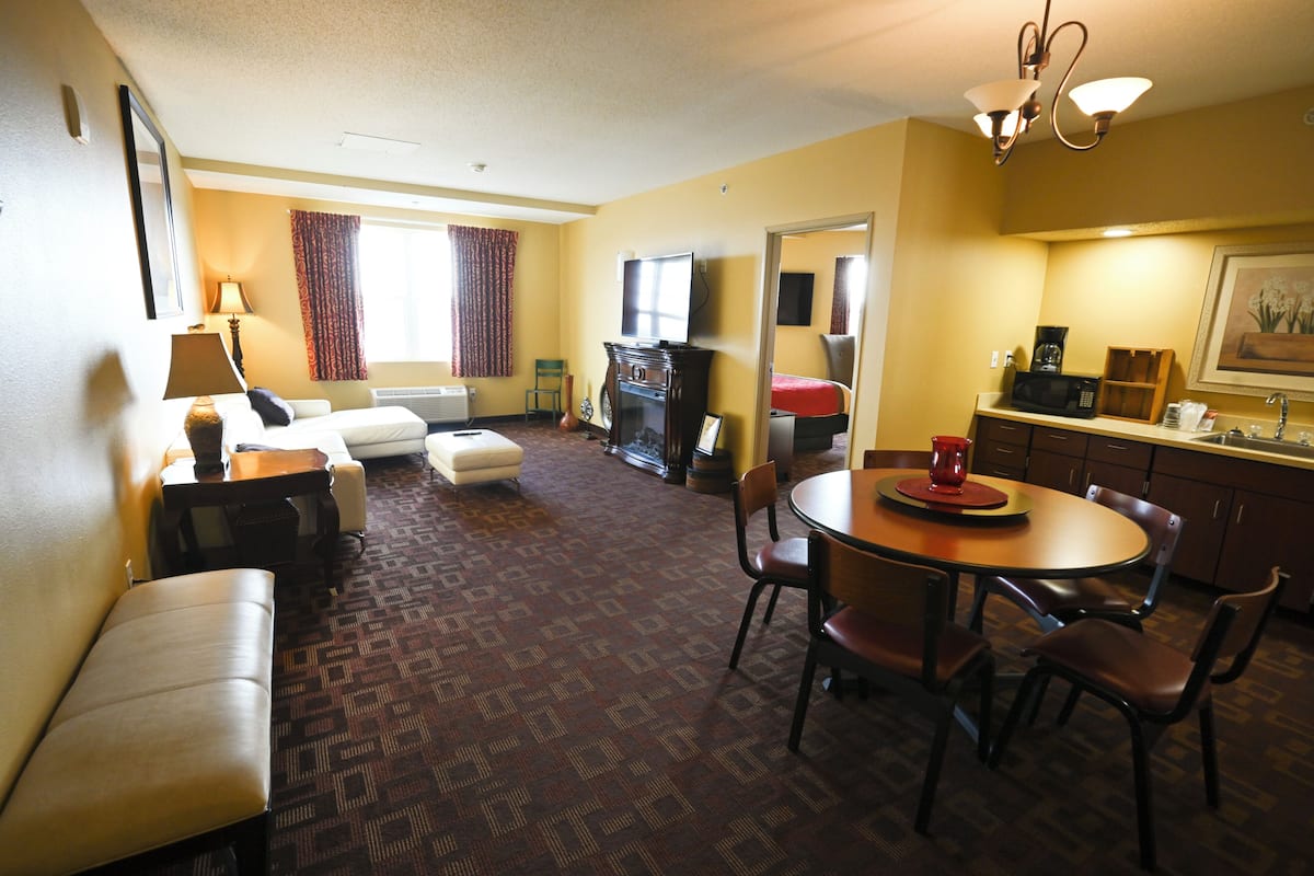 A hotel room with a sofa, a dining table with chairs, a kitchen area, and a television.