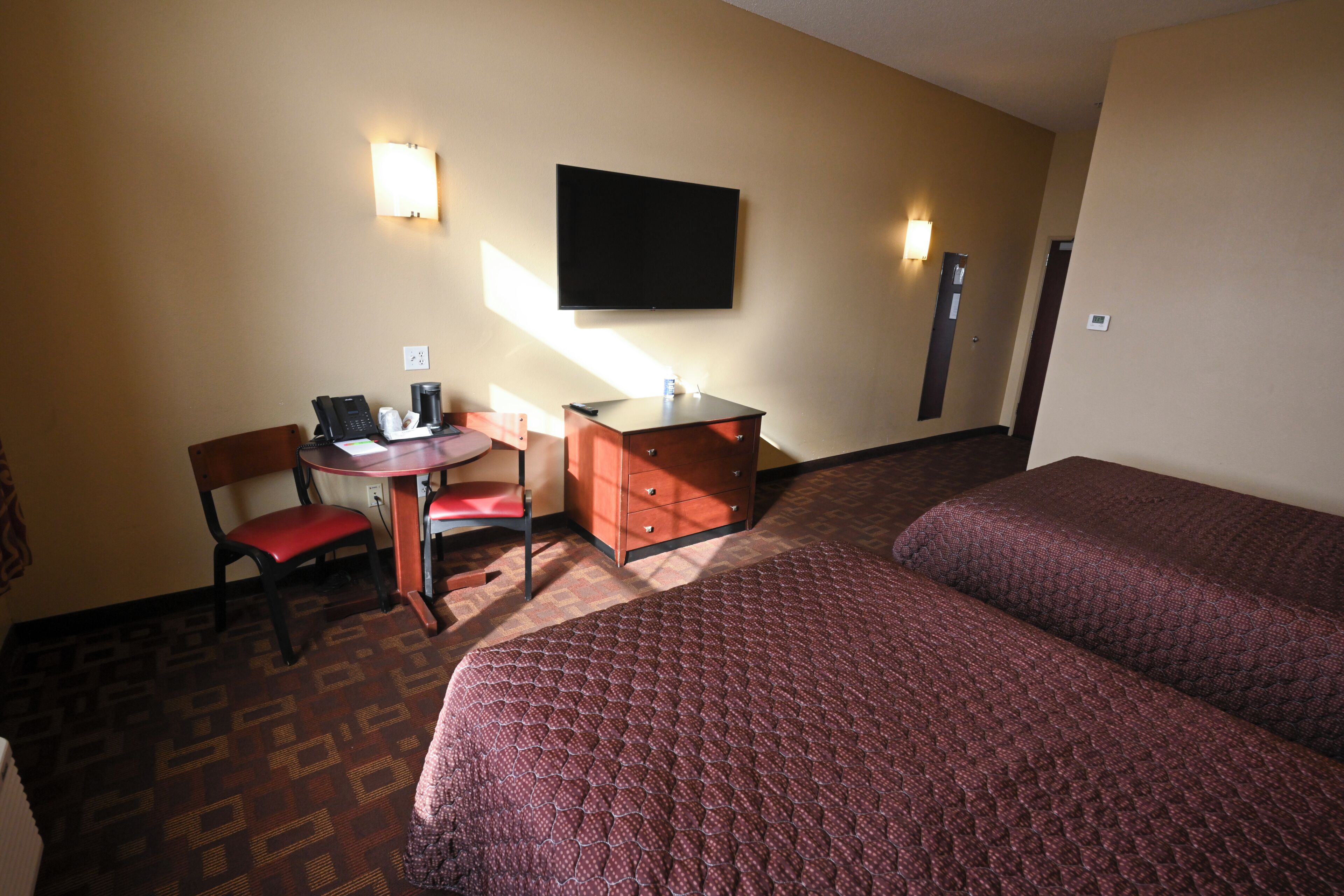 A hotel room with a bed, a desk with a chair, a telephone, and a flat-screen TV mounted on the wall.