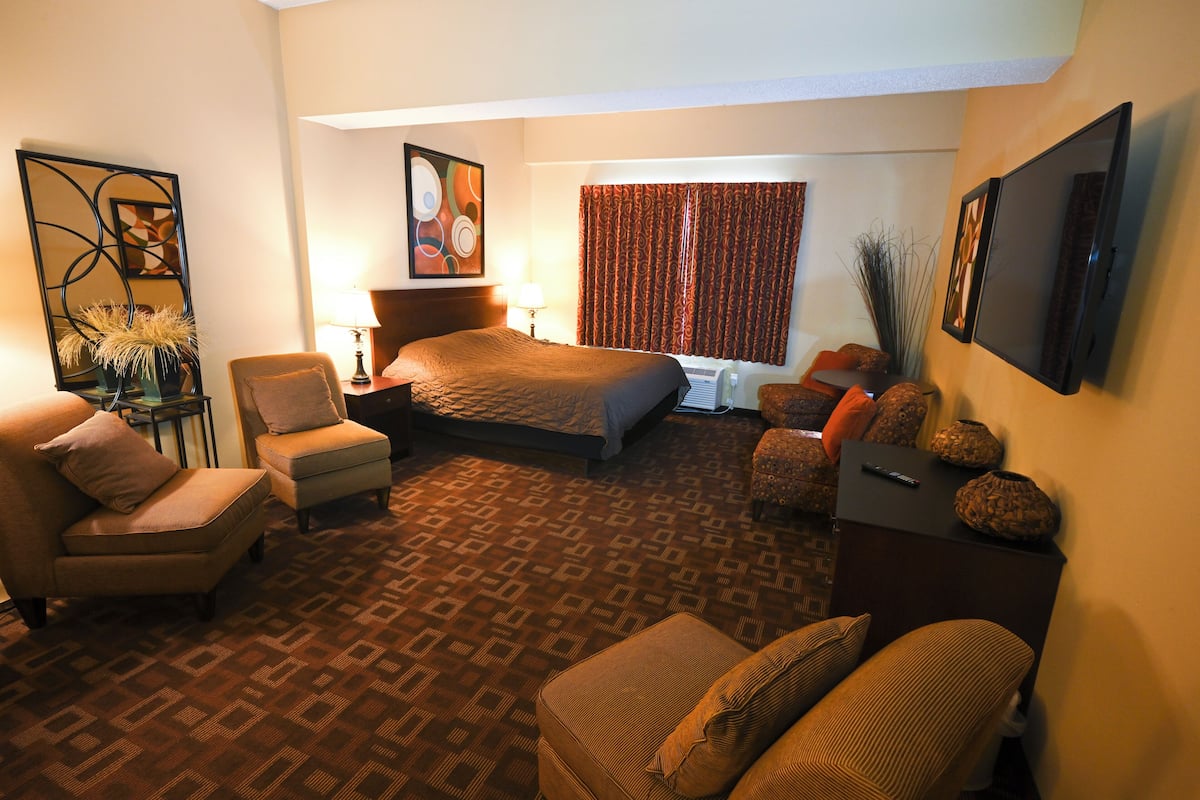 A hotel room with a large bed, two armchairs, a sofa, a small table, and a TV.