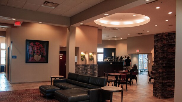 A lobby with a black leather sofa, a patterned carpet, a stone pillar, and a bar area in the background.