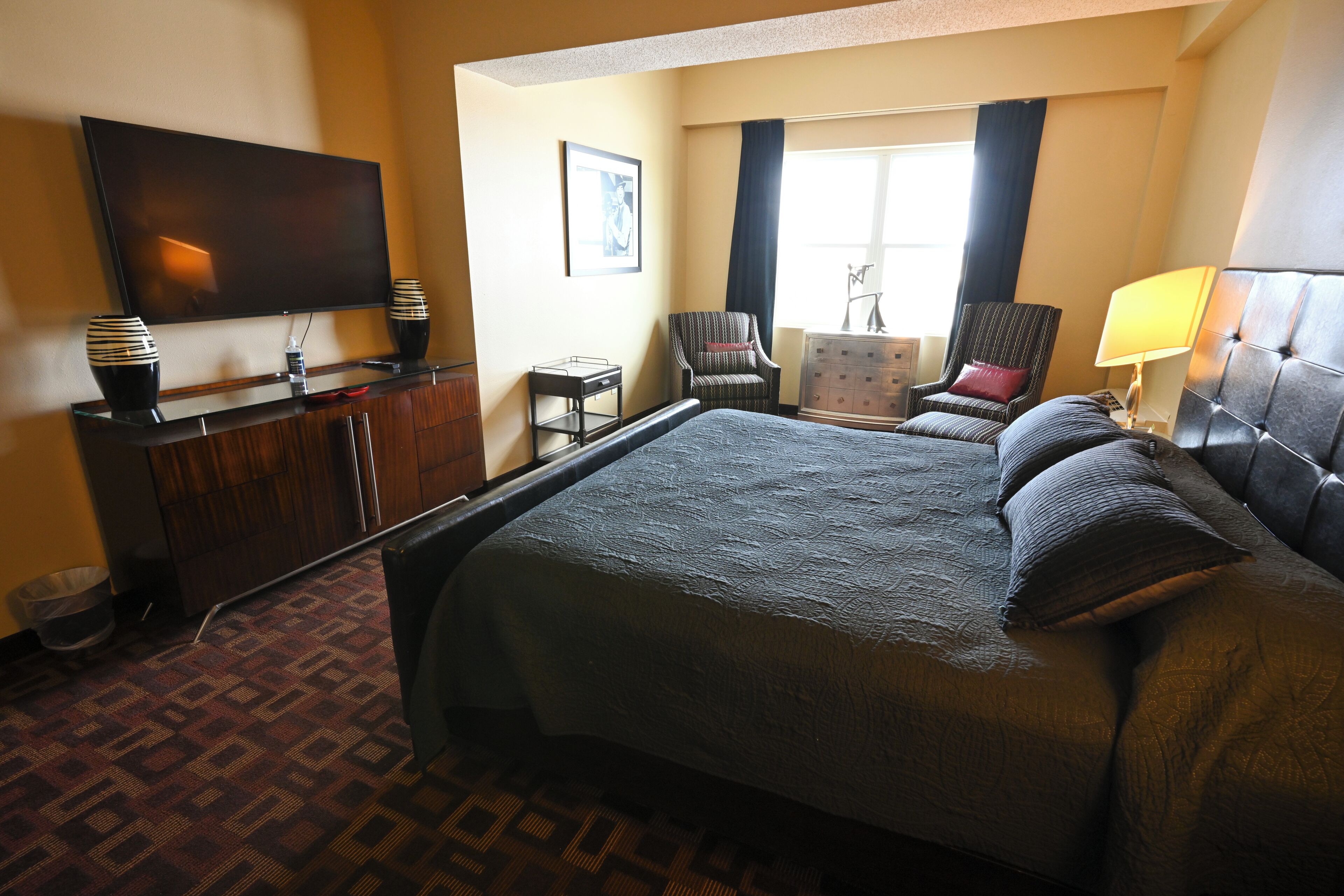 A hotel room with a large bed, a flat-screen TV, a desk with a lamp, and a chair.