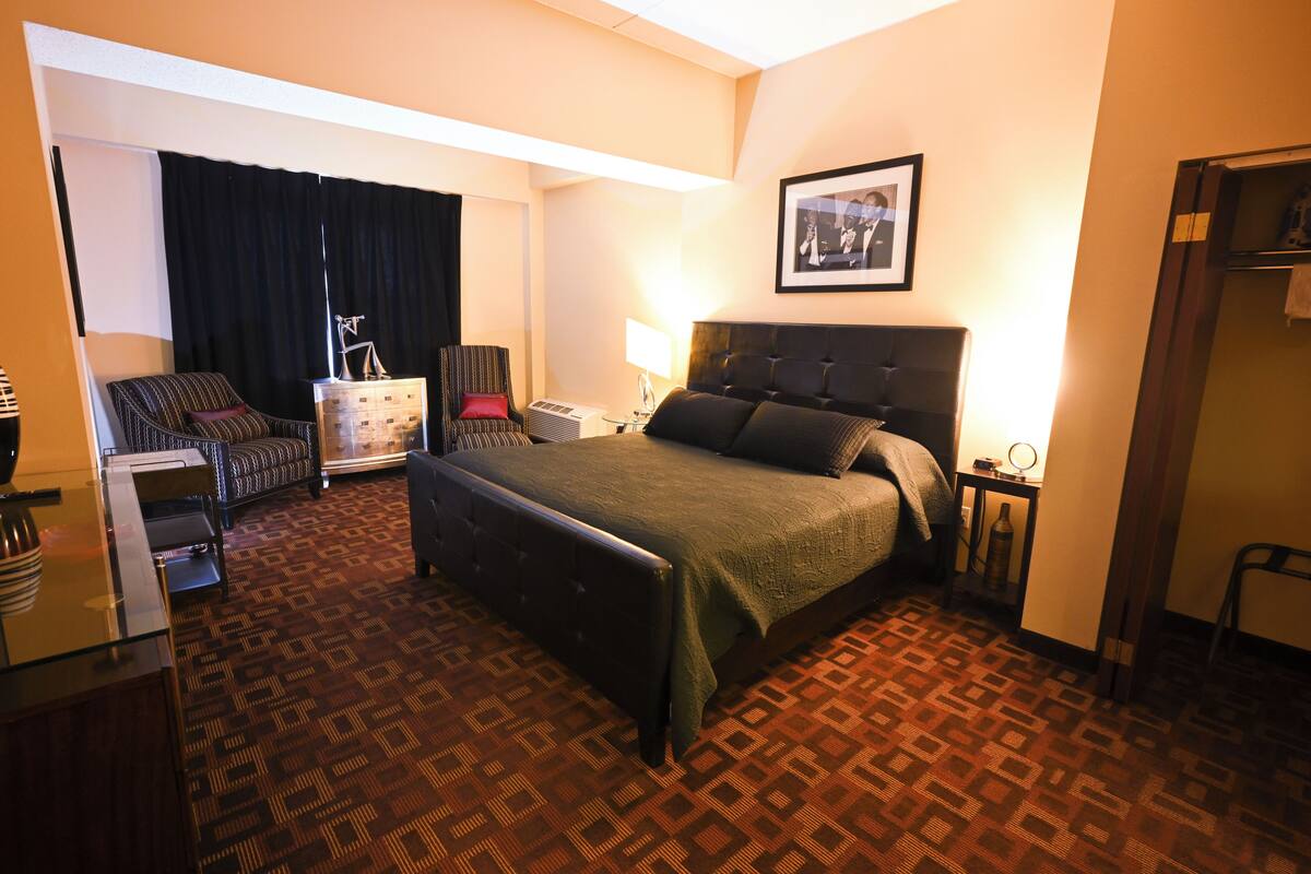 A hotel room with a bed, a chair, a desk, and a dresser.