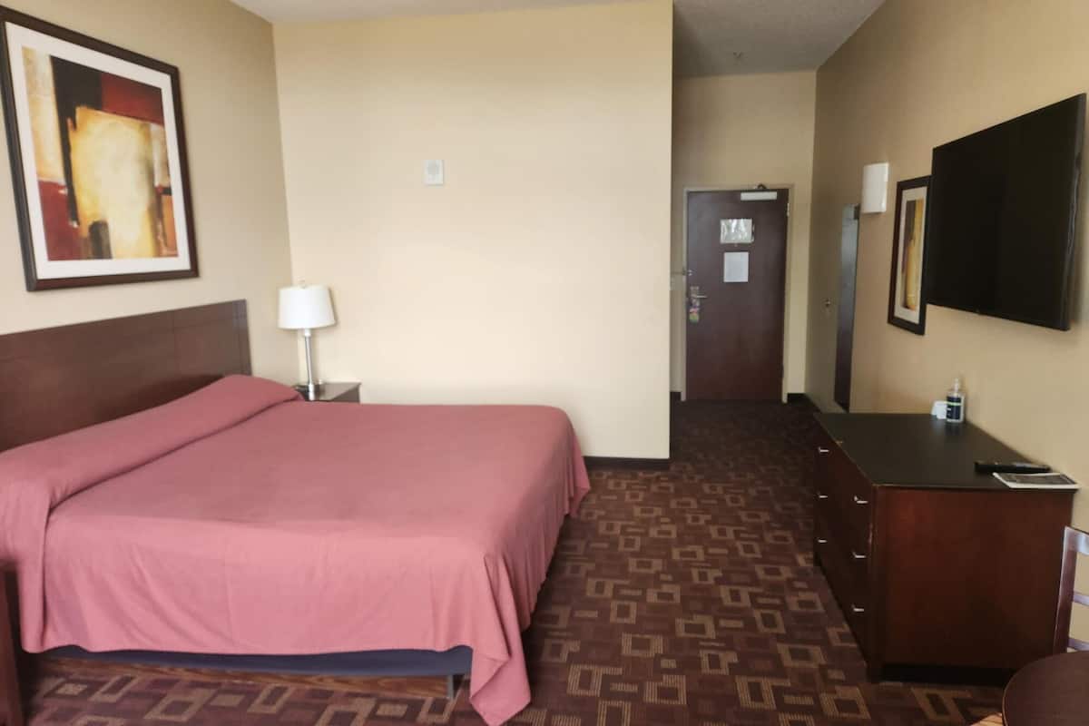 A hotel room with a large bed, a dresser, a desk, a television, and a door.