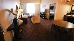 A hotel room with a sofa, armchair, dining table, and a TV.