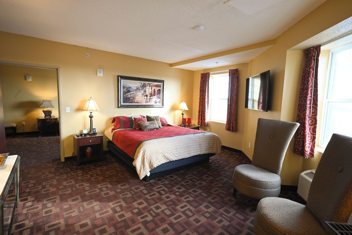 A hotel room with a bed, two nightstands, a chair, a TV, and a window with curtains.
