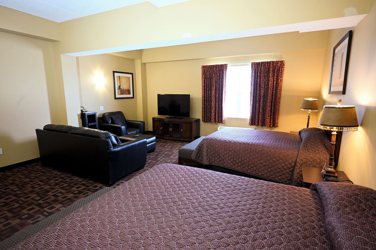 A hotel room with a sofa, two beds, a television, and a lamp.