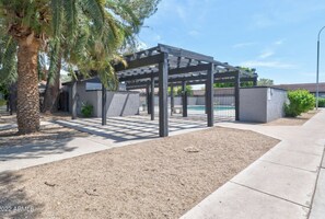 Relax under the shade of a pergola, adjacent to a swimming pool, amidst lush palm trees.
