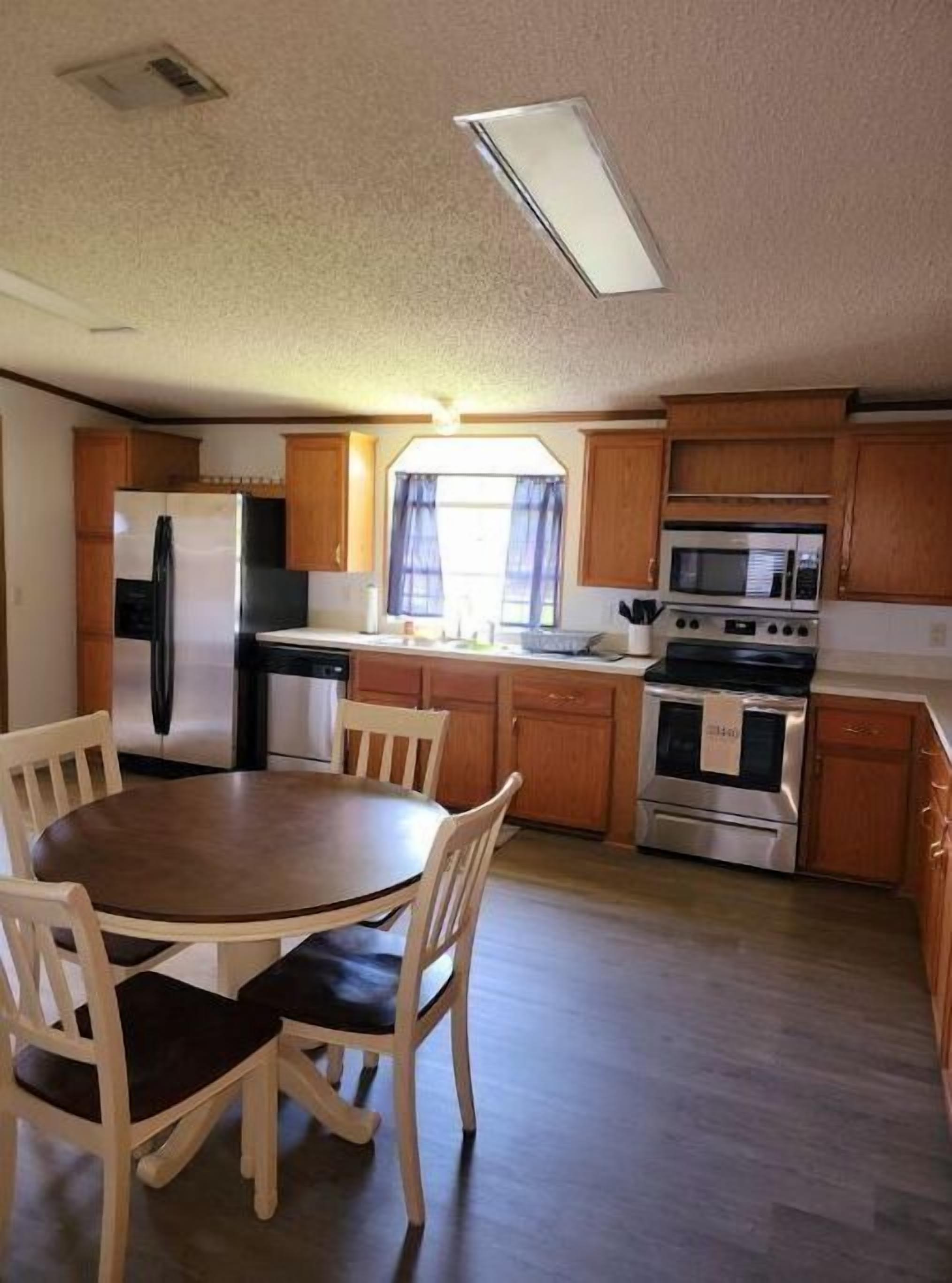 A compact kitchen with wooden cabinets, a refrigerator, a microwave, and an oven. There is a dining table with chairs.