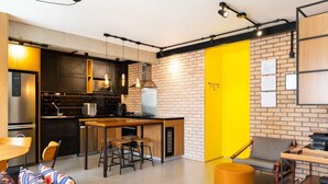 A modern kitchen with a brick wall, a yellow accent wall, and a dining area with a wooden table and chairs. - Apto Peixoto Gomide (São Paulo)