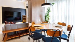 A modern living room with a sofa, a dining table set for four, and a TV mounted on the wall. - Apto Peixoto Gomide (São Paulo)