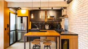 A modern kitchen with a central island, bar stools, stainless steel appliances, and a brick wall. - Apto Peixoto Gomide (São Paulo)
