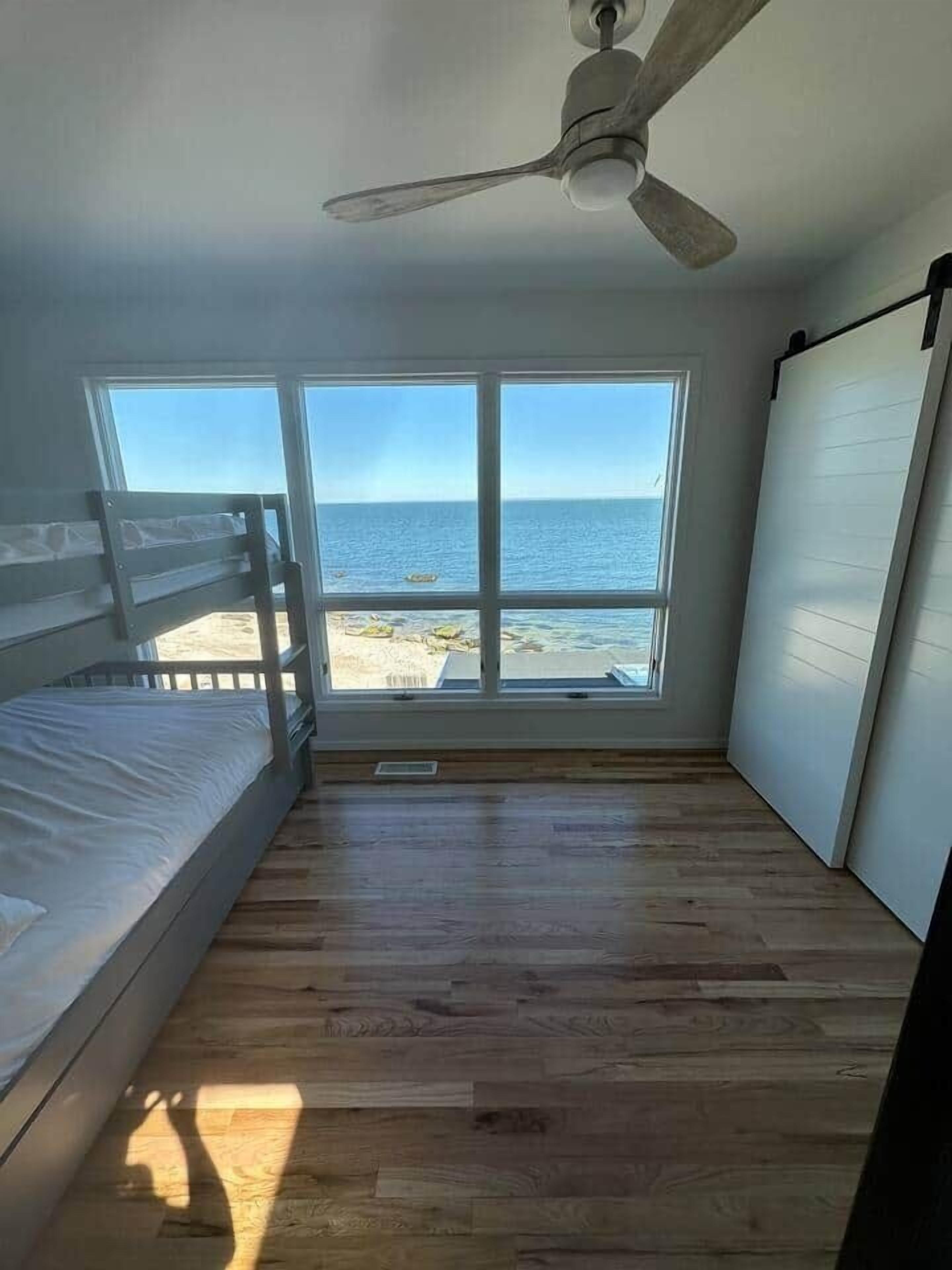 Ein Zimmer mit Etagenbett, großen Fenstern mit Meerblick und Deckenventilator.