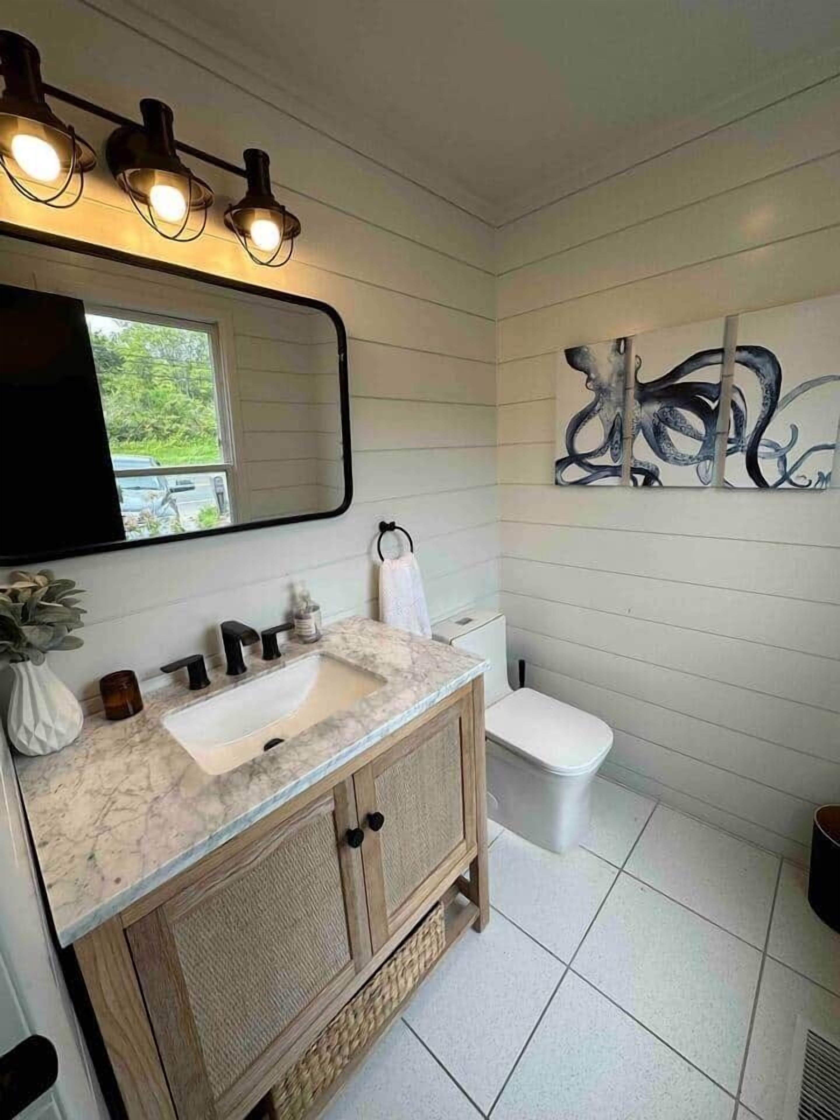 Un baño con tocador blanco, un espejo grande y un aplique en la pared.