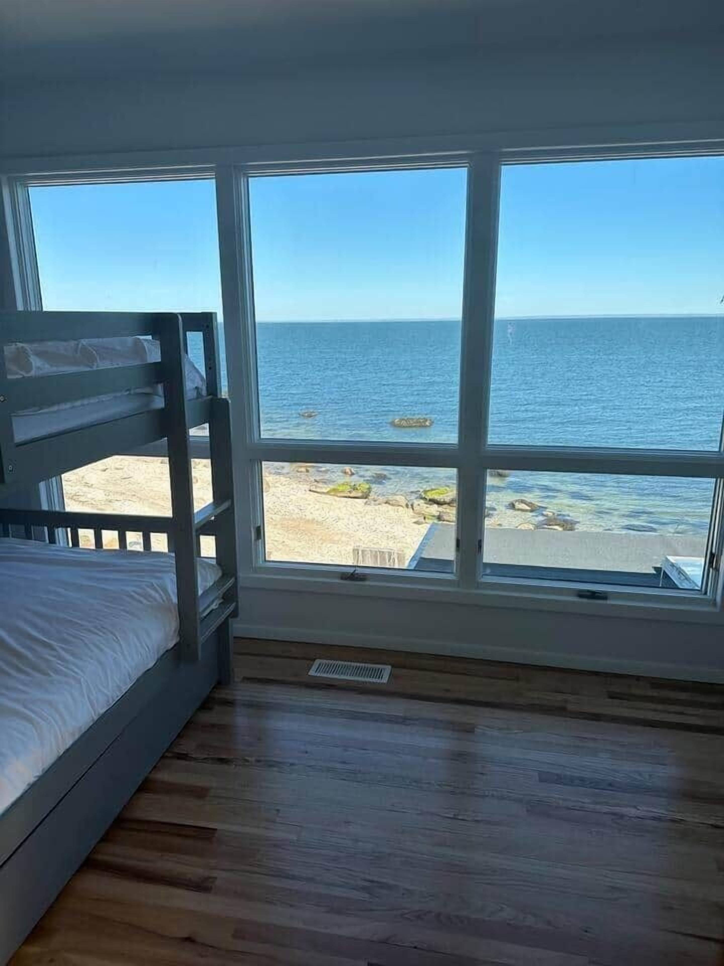 A room with a bunk bed and a large window overlooking a beach and ocean.