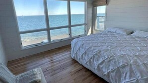 A bedroom with a large bed, a ceiling fan, and a view of the ocean through large windows.