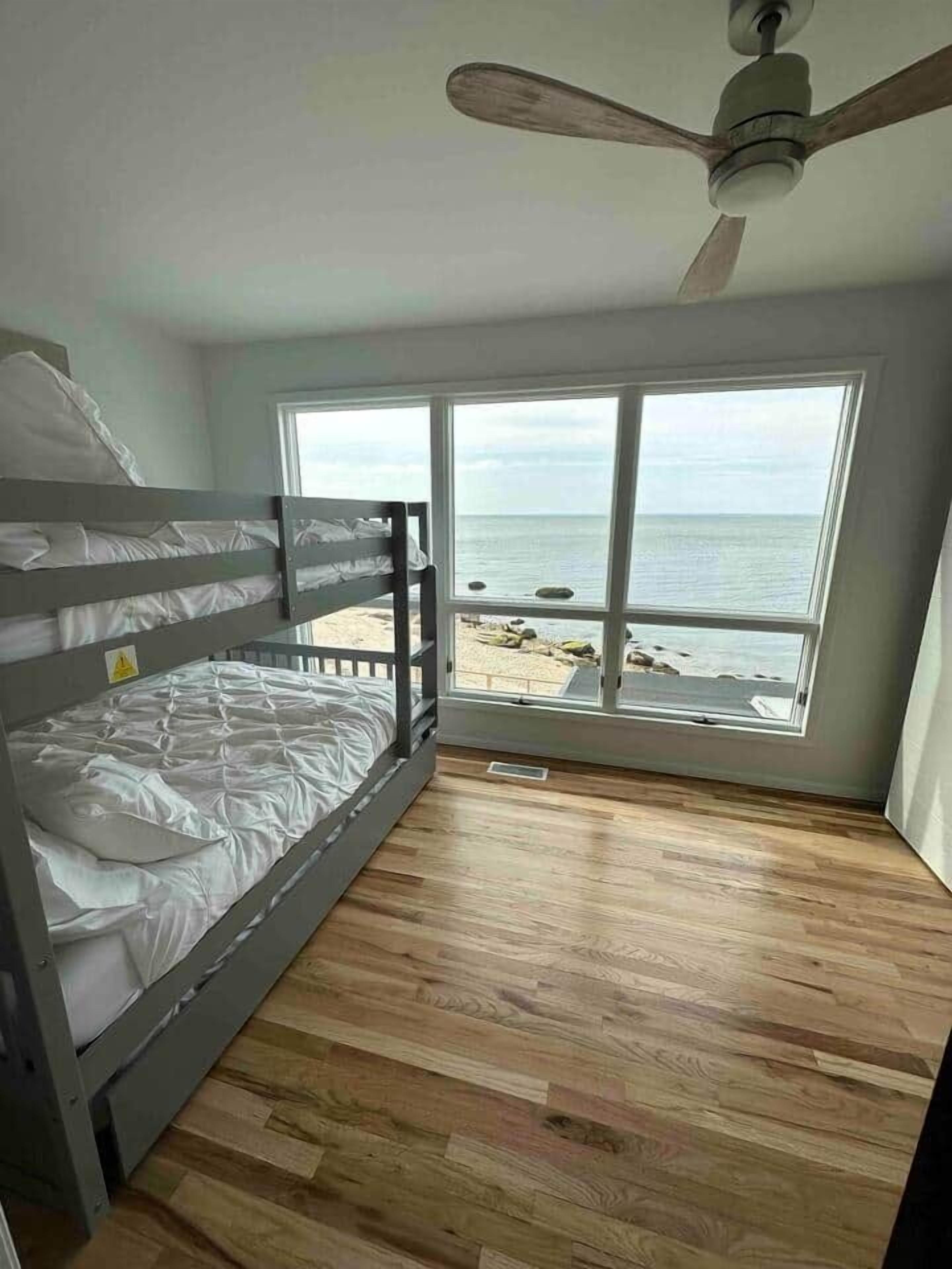 Ein Zimmer mit Etagenbett, Deckenventilator und großem Fenster mit Blick auf einen Strand.
