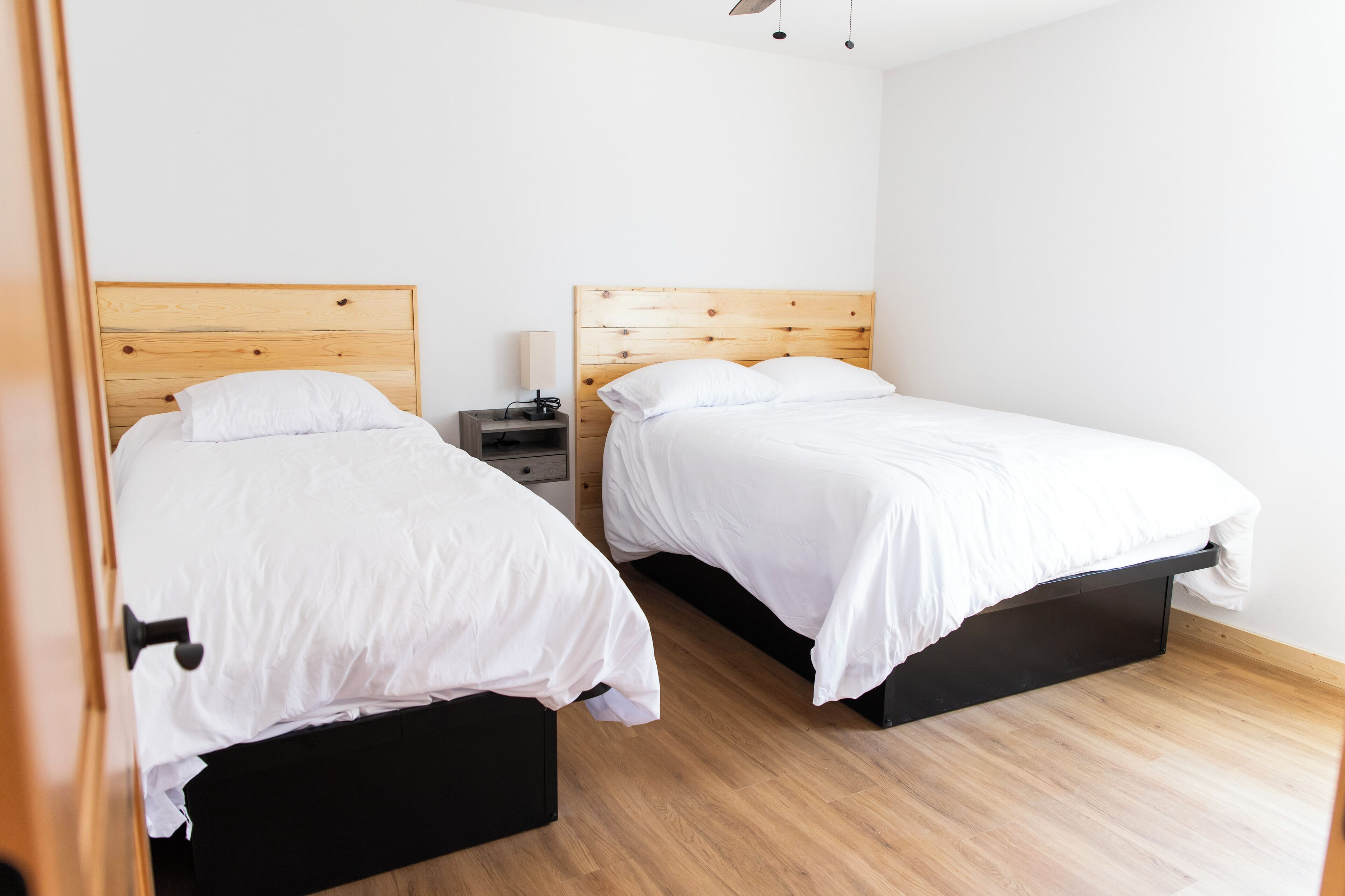 A bedroom with two beds, a nightstand, and a wooden headboard.