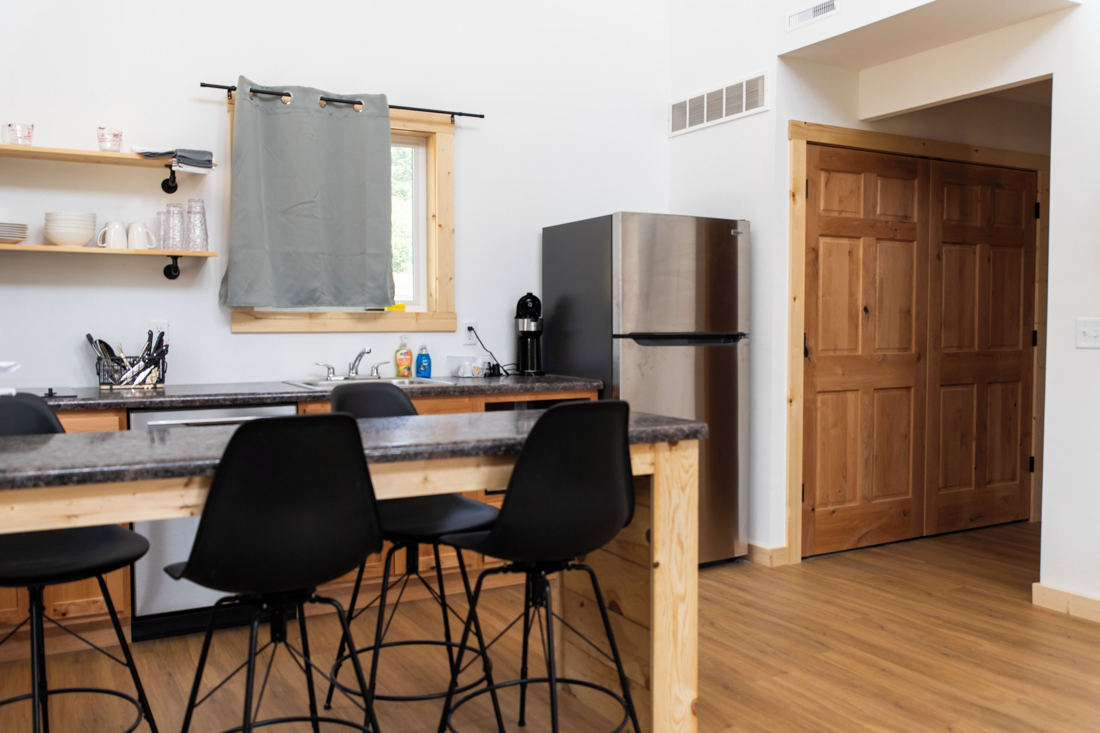 A kitchen with a wooden countertop, black chairs, a stainless steel refrigerator, and a wooden door.