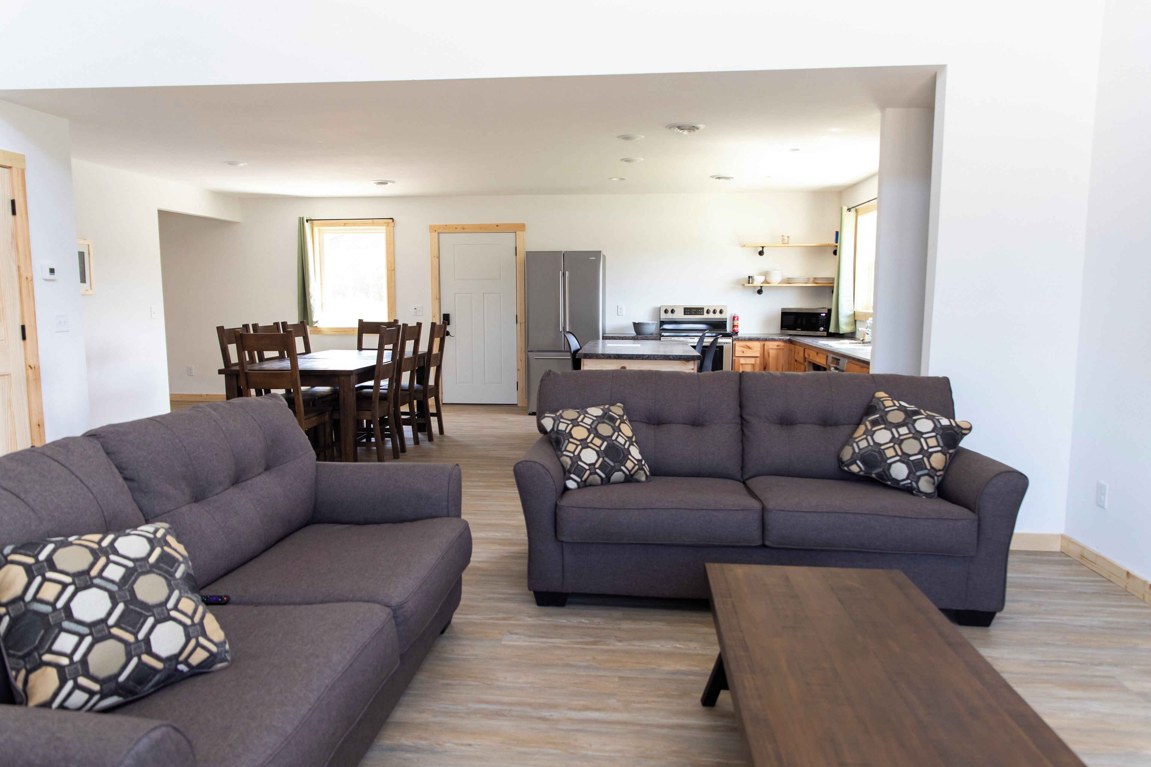 A living room with two sofas and a wooden coffee table, a dining area with a table and chairs, and a kitchen in the background.
