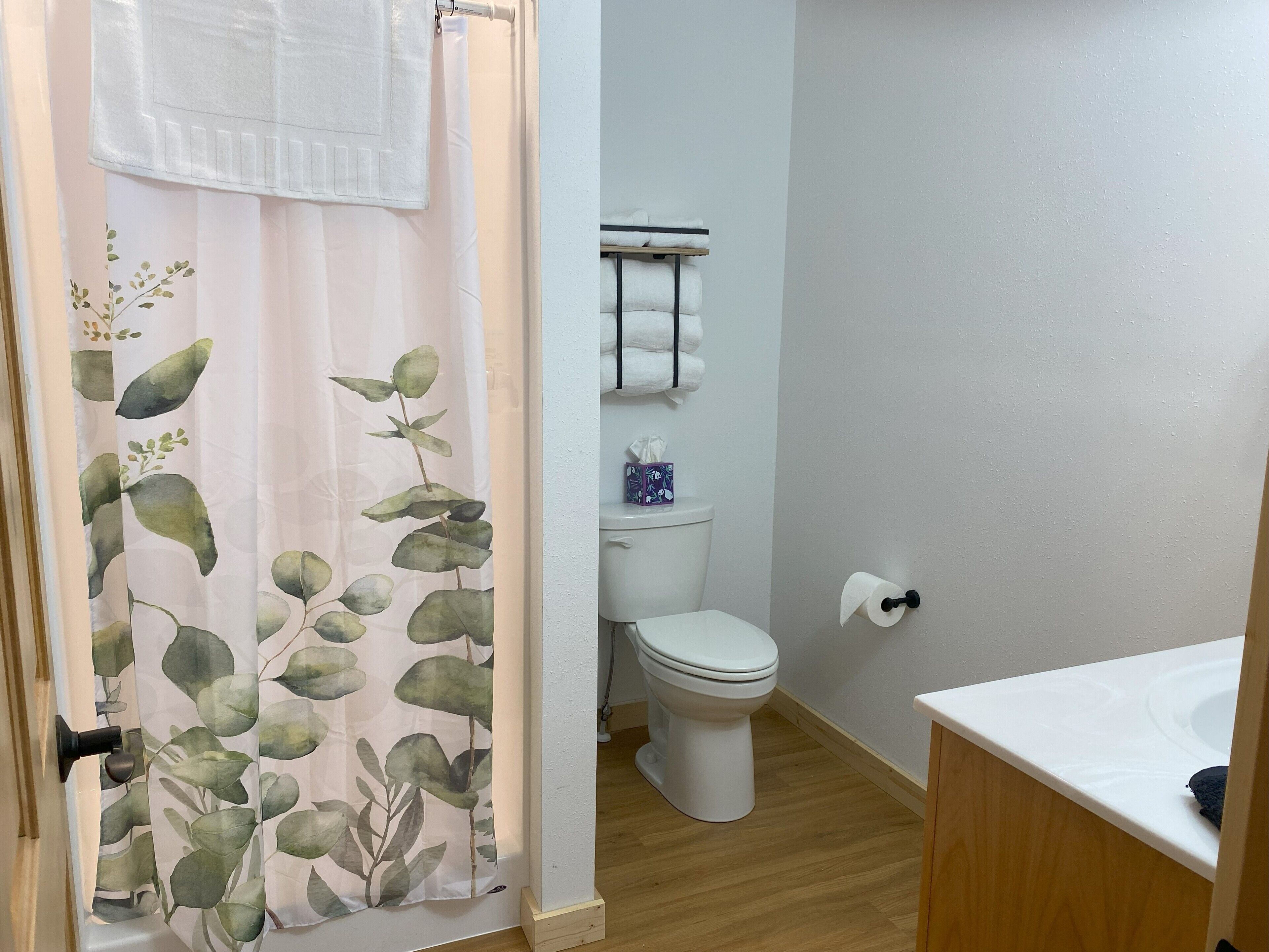 Un baño con inodoro, lavabo y cortina de ducha con estampado de hojas.