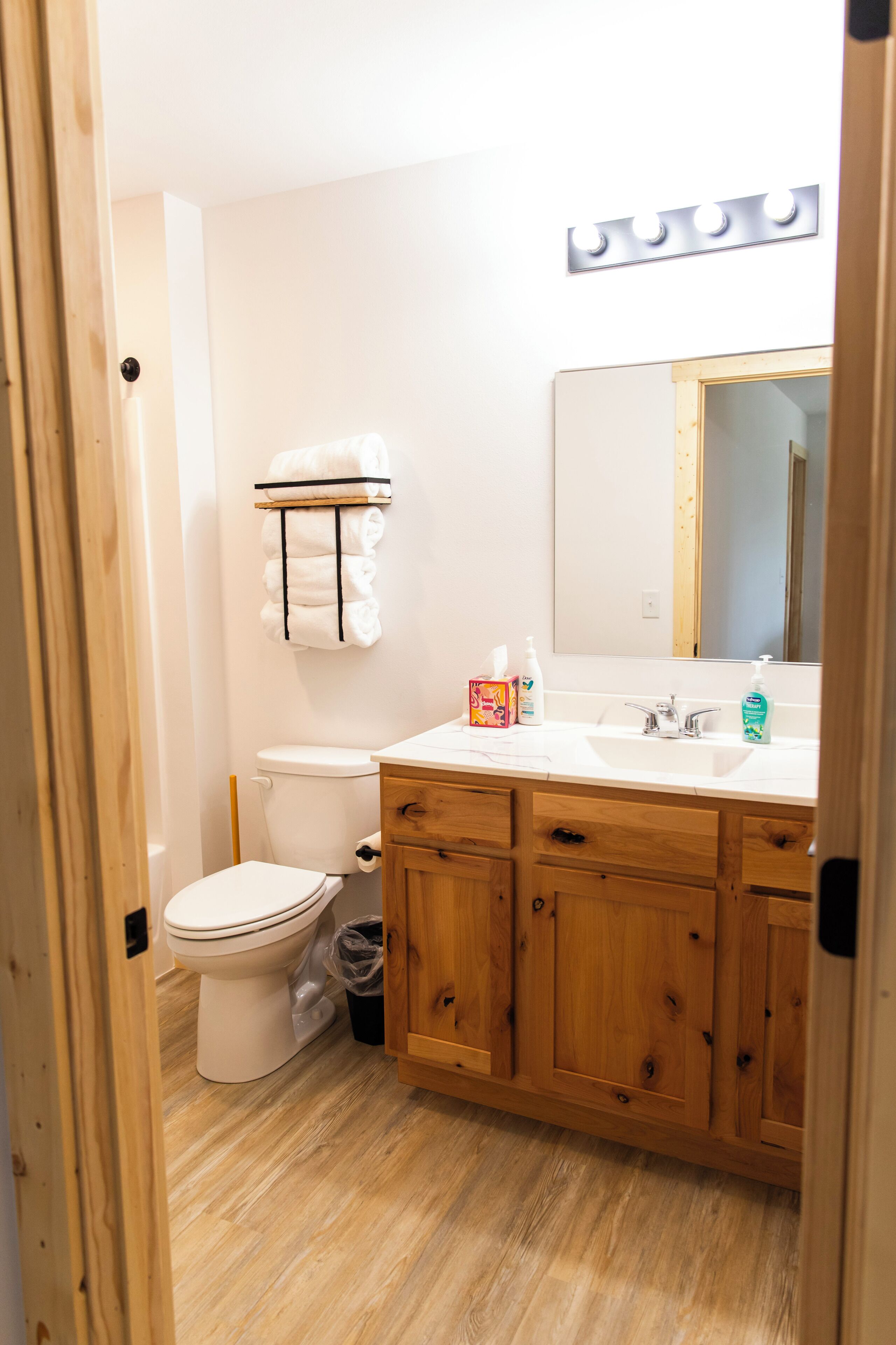 A bathroom with a white toilet, wooden cabinets, a vanity with a mirror, and a towel rack.