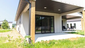 A modern building with a covered patio area, large sliding glass doors, and outdoor seating. - Bluffside Gardens (Decorah)