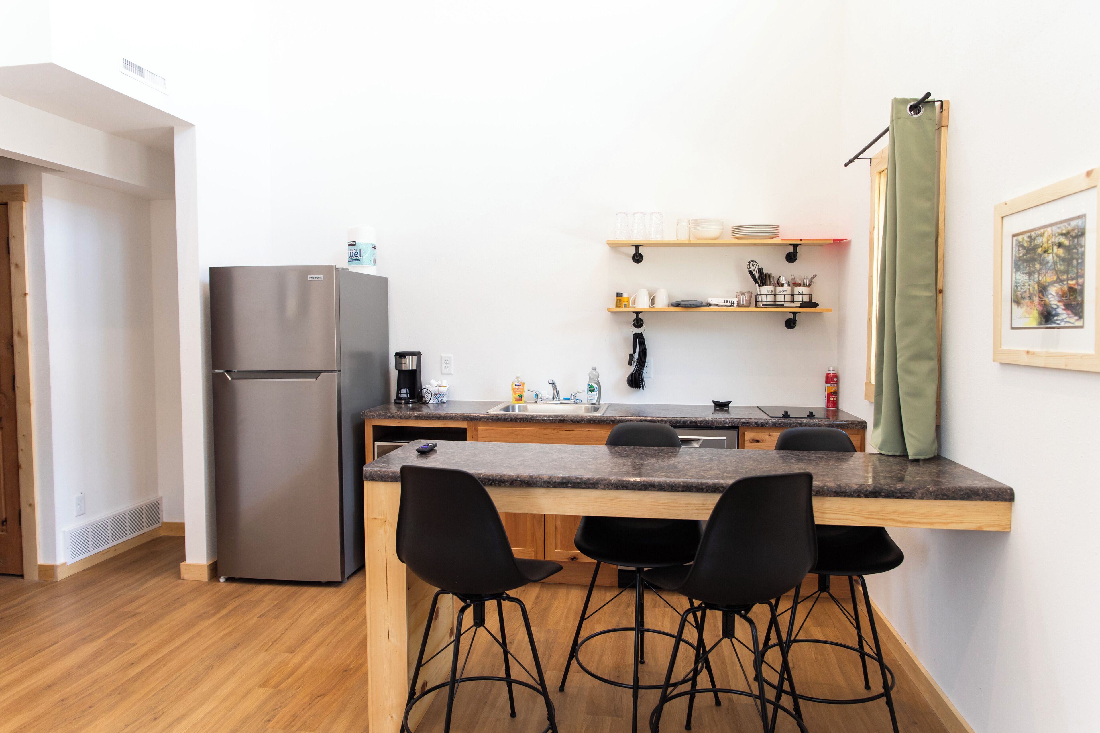 Een kleine keuken met een koelkast, een spoelbak en barstoelen.
