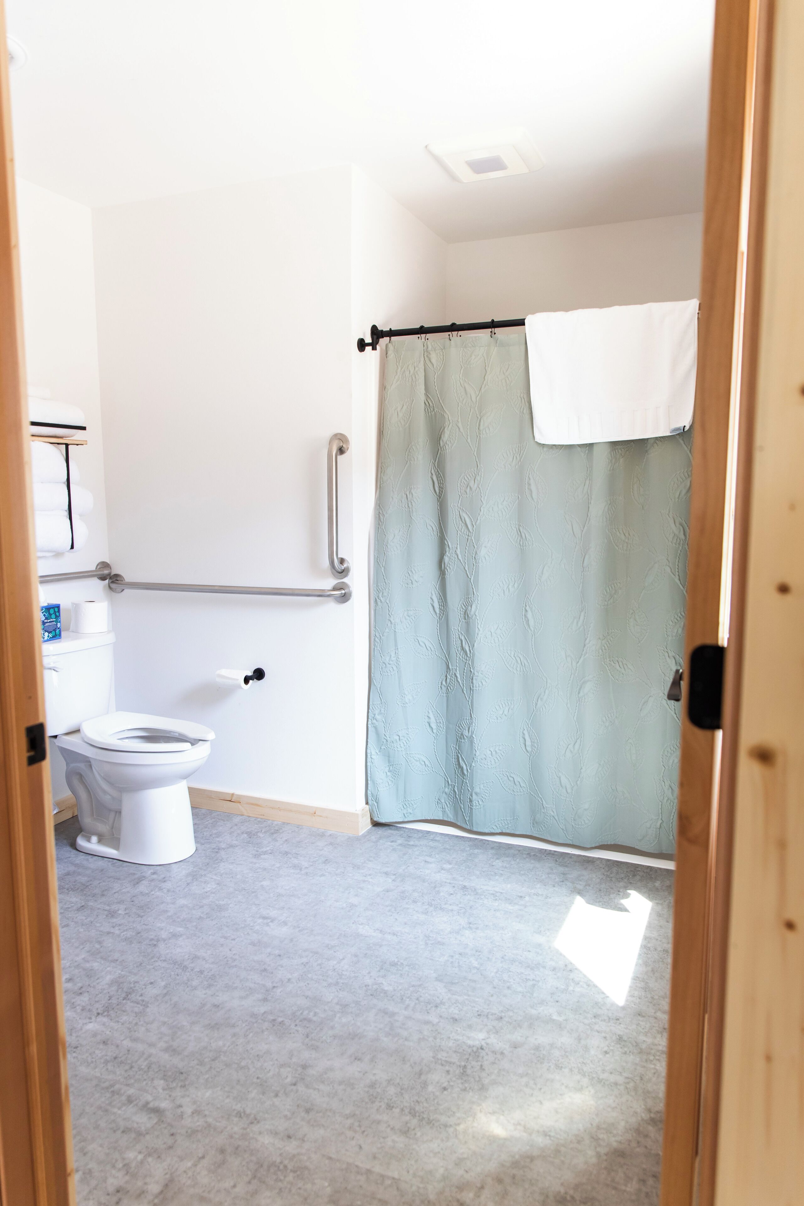 Un baño con inodoro blanco, cortina de ducha y barra de apoyo.