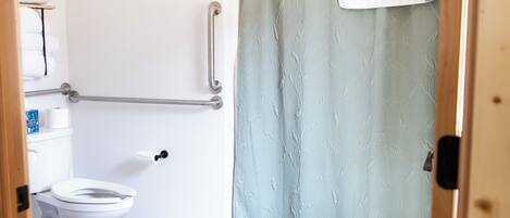 Un baño con inodoro blanco, cortina de ducha y barra de apoyo.