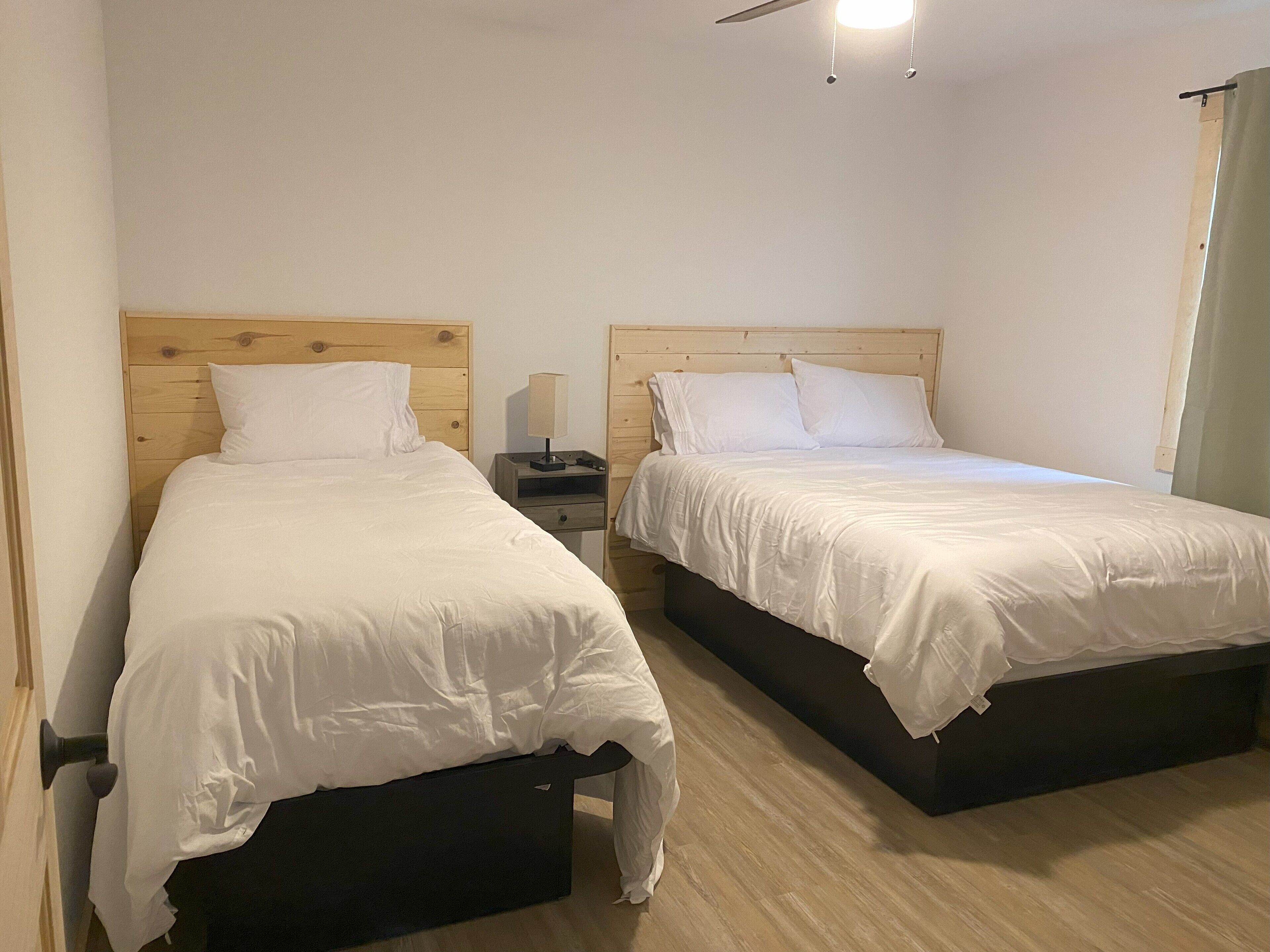 Two single beds with wooden headboards, a bedside table with a lamp, and a ceiling fan.