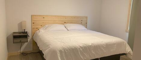 Un dormitorio con cabecera de madera, cama con ropa de cama blanca, mesita de noche con lámpara y ventilador de techo.