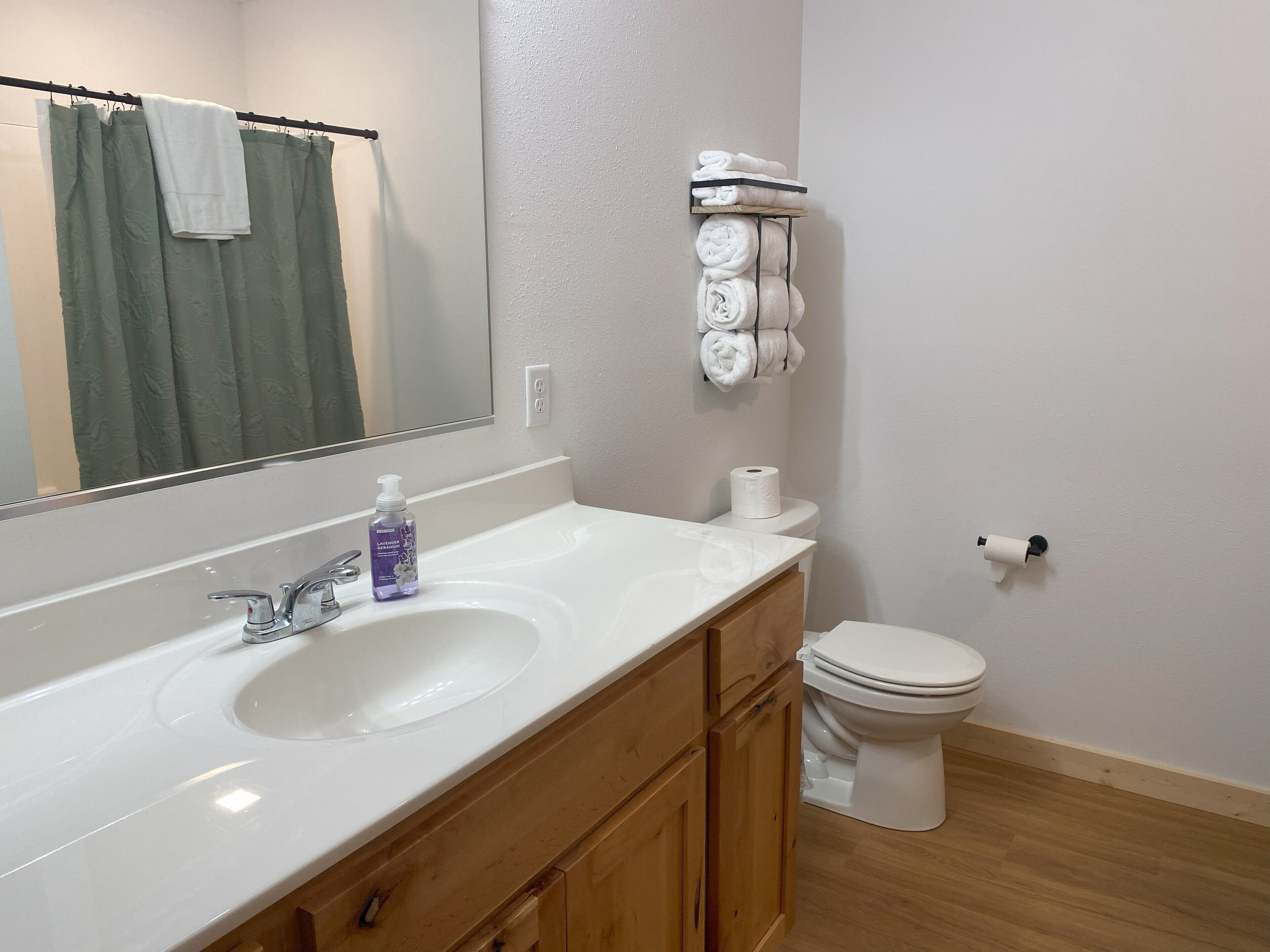 A bathroom with a white sink, wooden cabinets, a mirror, a toilet, and a towel rack with towels.