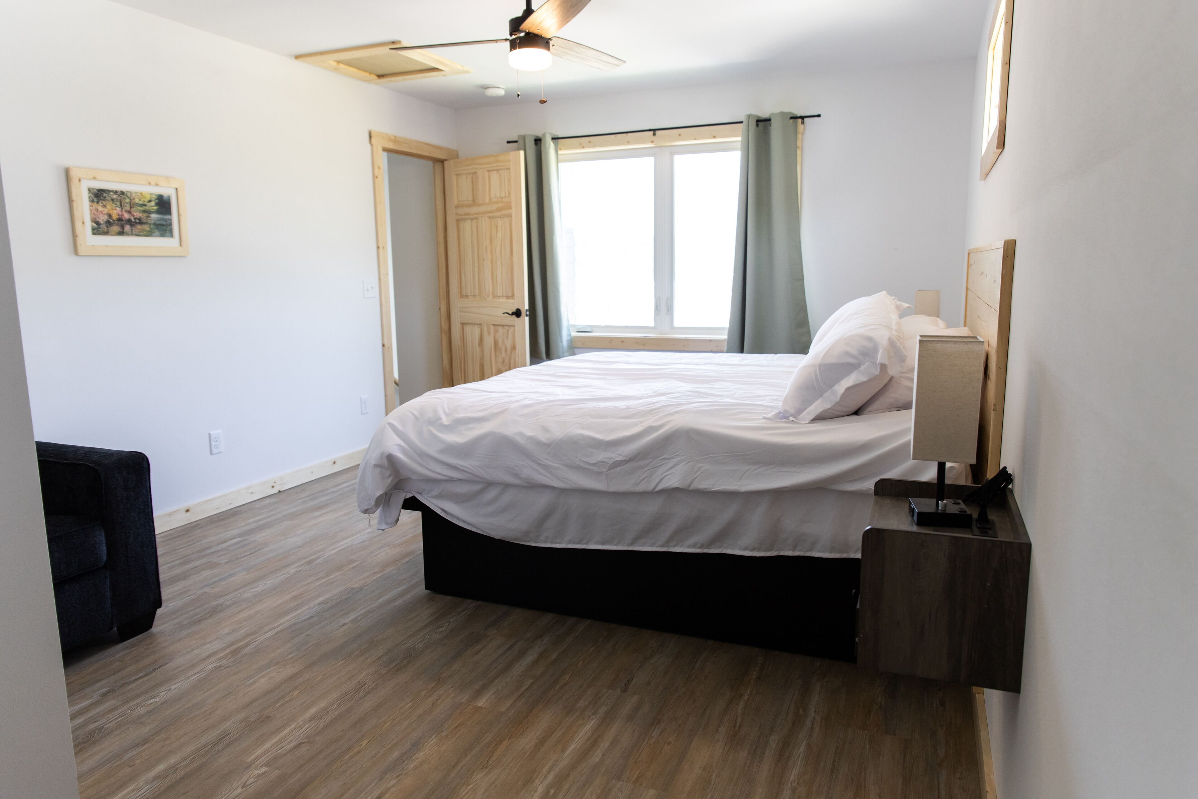 Un dormitorio con cama, mesita de noche, ventilador de techo, ventana con cortinas y puerta.