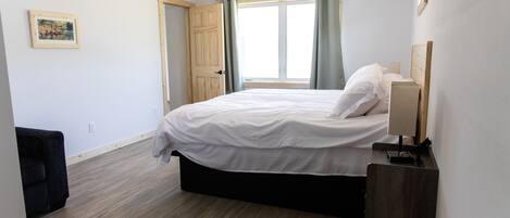 Un dormitorio con cama, mesita de noche, ventilador de techo, ventana con cortinas y puerta.