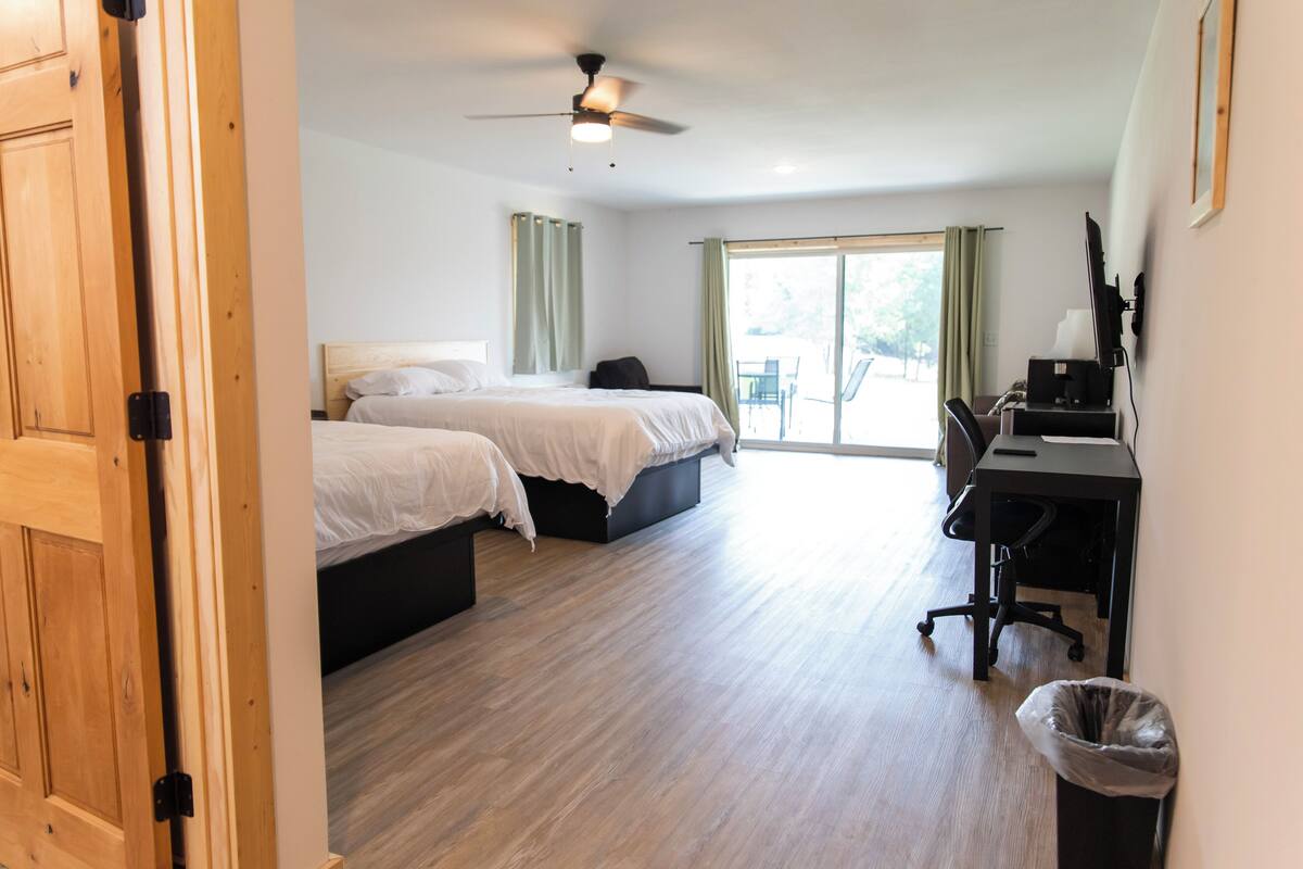 Hotellihuone, jossa on kaksi sänkyä, työpöytä, tuoli, kattotuuletin ja näkymä ulos.