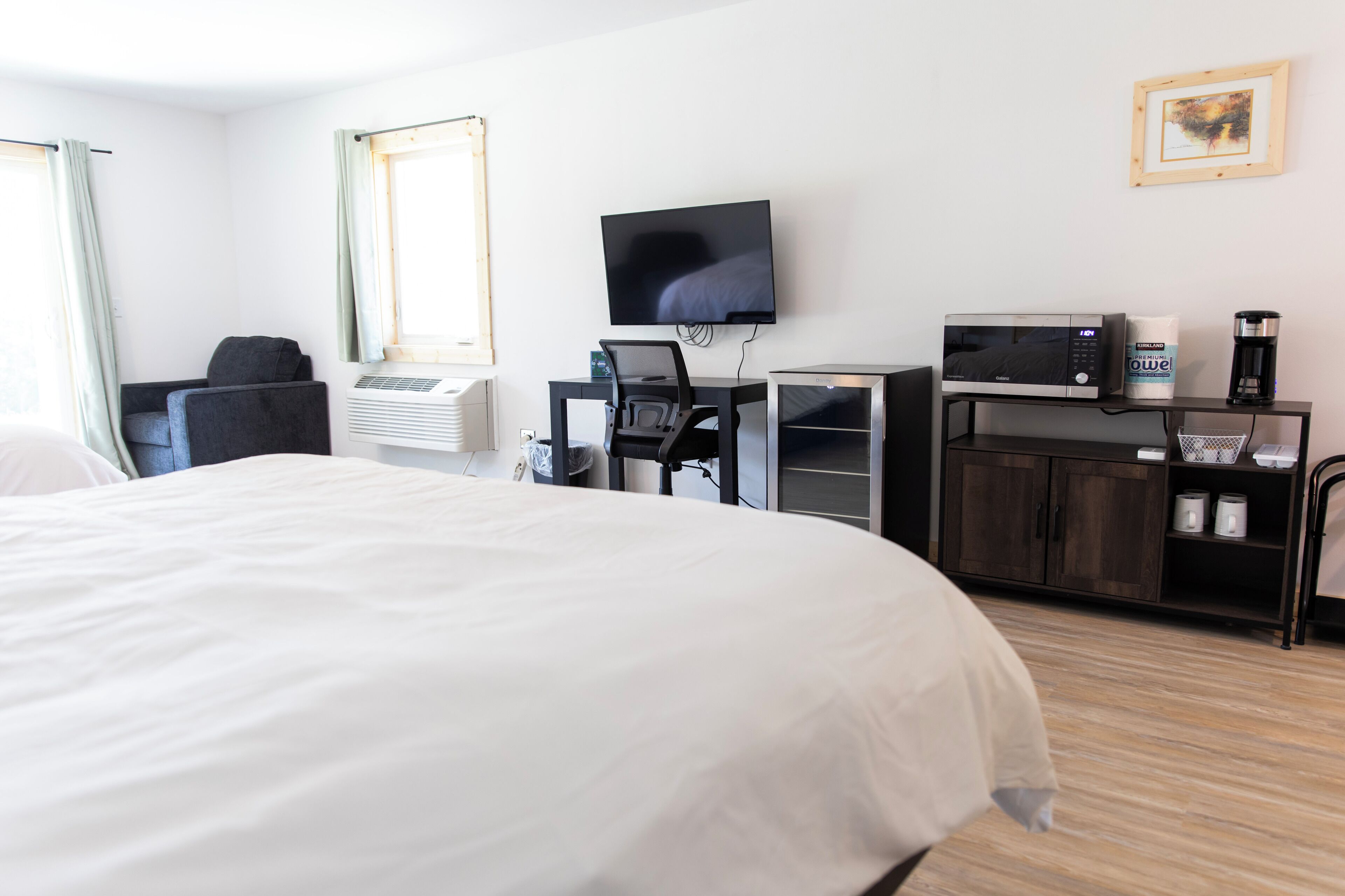 Habitación de hotel con una cama grande, un escritorio con computadora, televisor, microondas y cafetera.