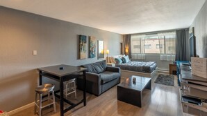 Una habitación de hotel compacta con cama, sofá, escritorio y una pequeña zona de comedor.