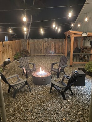 A patio area with a fire pit surrounded by chairs, a wooden fence, and a bike lane sign. - Beautiful home in Grand Junction, everything you need and more!  (Grand Junction)
