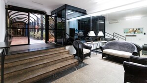 Ein modernes Interieur mit einer Treppe, die zu einem Balkon führt, schwarzen Korbmöbeln und einer Glastrennwand.