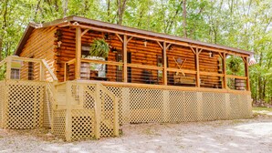 Una cabaña de madera con porche, rodeada de árboles.