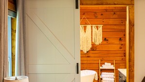 Un dormitorio acogedor con una cama, una mesita de noche, una lámpara y una puerta corrediza que da a un baño con bañera y toallas.