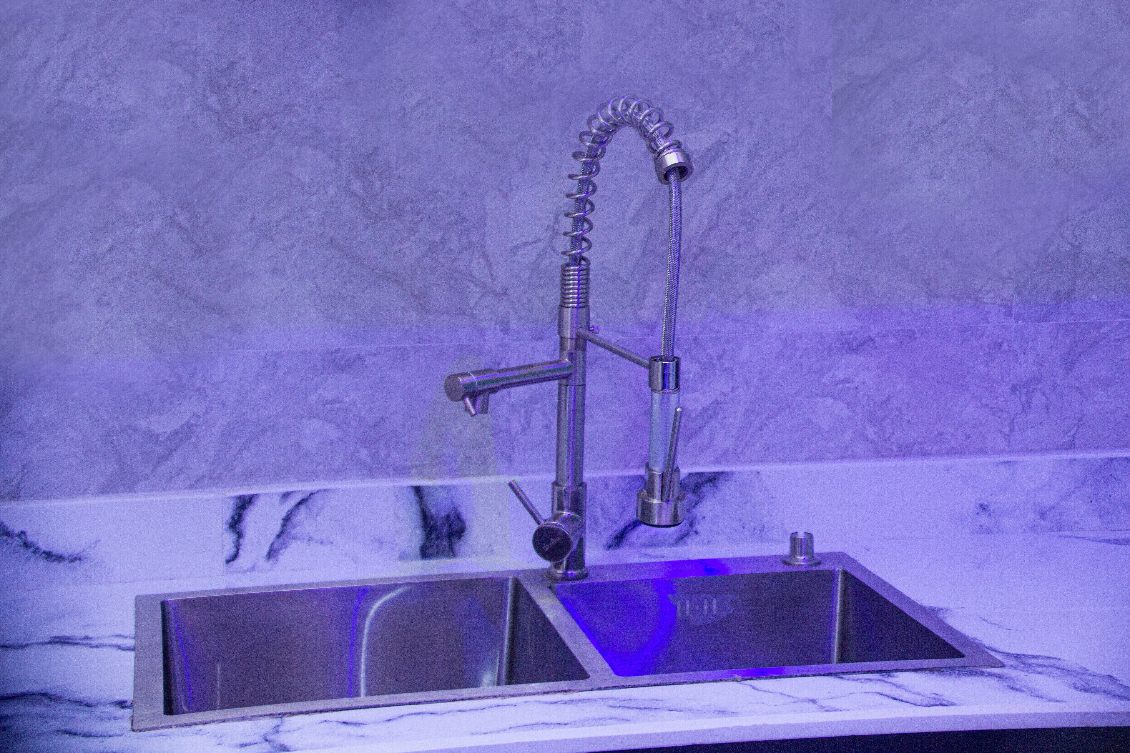 A modern kitchen with a stainless steel sink, a double faucet, and a marble countertop.
