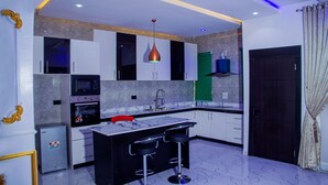 A modern kitchen with a central island, bar stools, a microwave, and a built-in oven. - RichVilla Apartments & Hotels (Lagos)